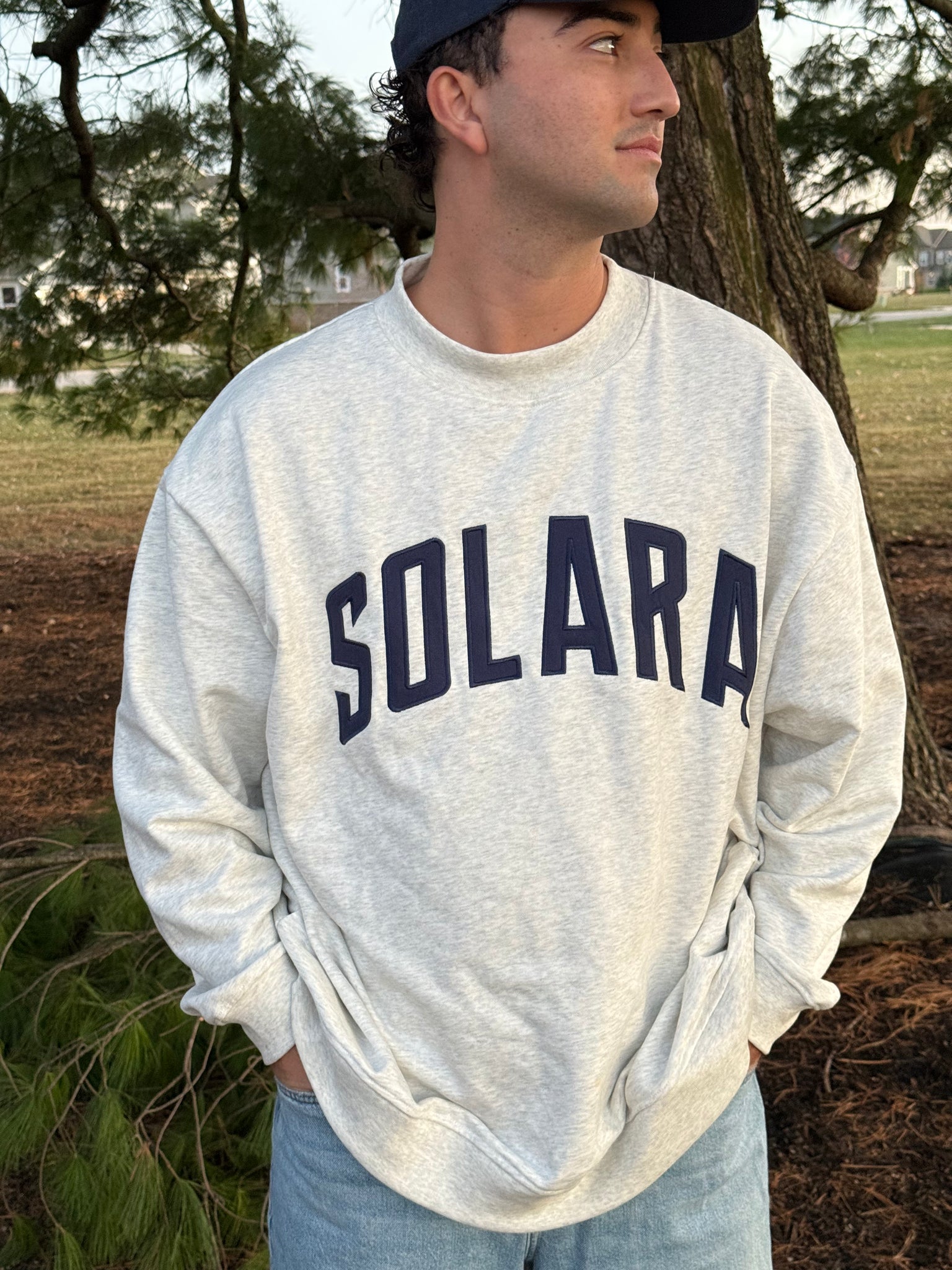 Person wearing a gray sweatshirt with 'SOLARA' printed on it, standing outdoors.